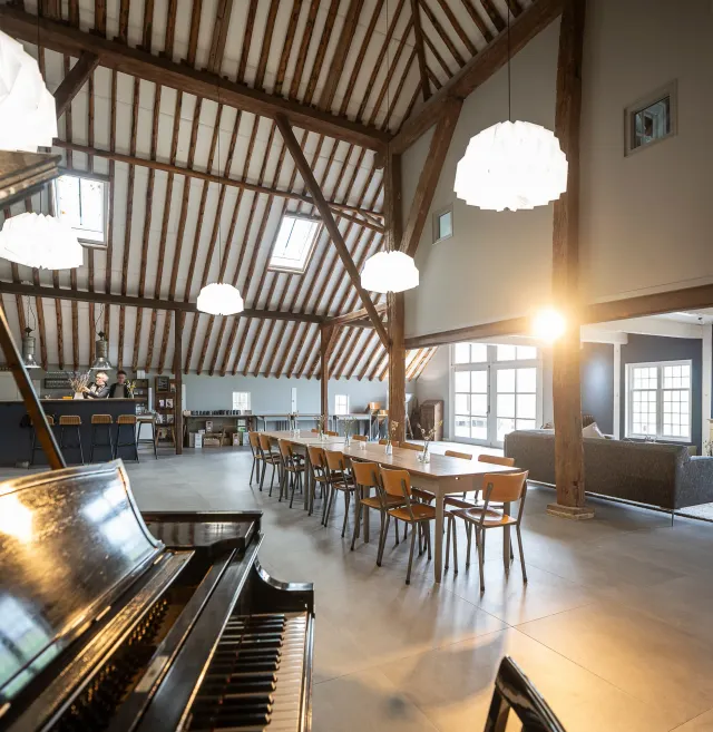 Groepsaccommodatie Nynke's Pleats in Piaam van de binnenkant met een piano op de voorgrond en een lange tafel met 15 stoelen.