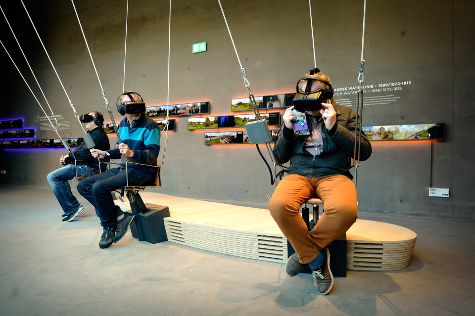 Mensen zitten op een speciale schommel en dragen een VR-bril.