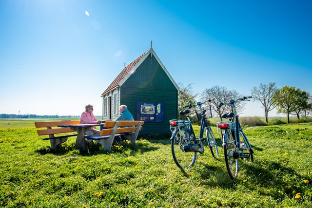 Een echtpaar zit aan een picknicktafel op Schokland in de Noordoostpolder met hun fietsen voor hun uitgestald.