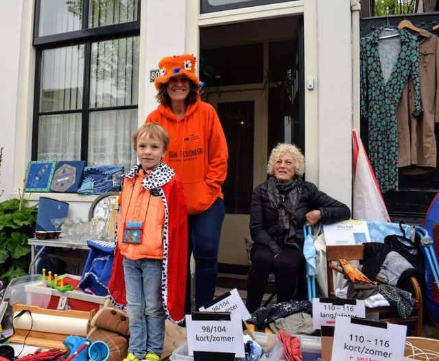 Twee vrouwen en een jongen die verkleed spullen verkopen op de rommelmarkt tijdens Koningsdag