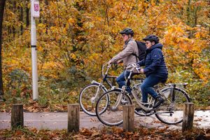 Twee personen aan het fietsen door een herfstbos met helmen op.