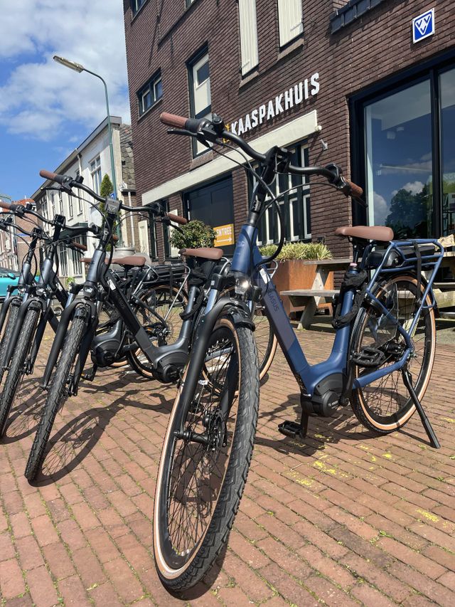 E-bikes voor de verhuur bij VVV Woerden, geparkeerd voor het VVV/Kaaspakhuis op een zonnige dag.