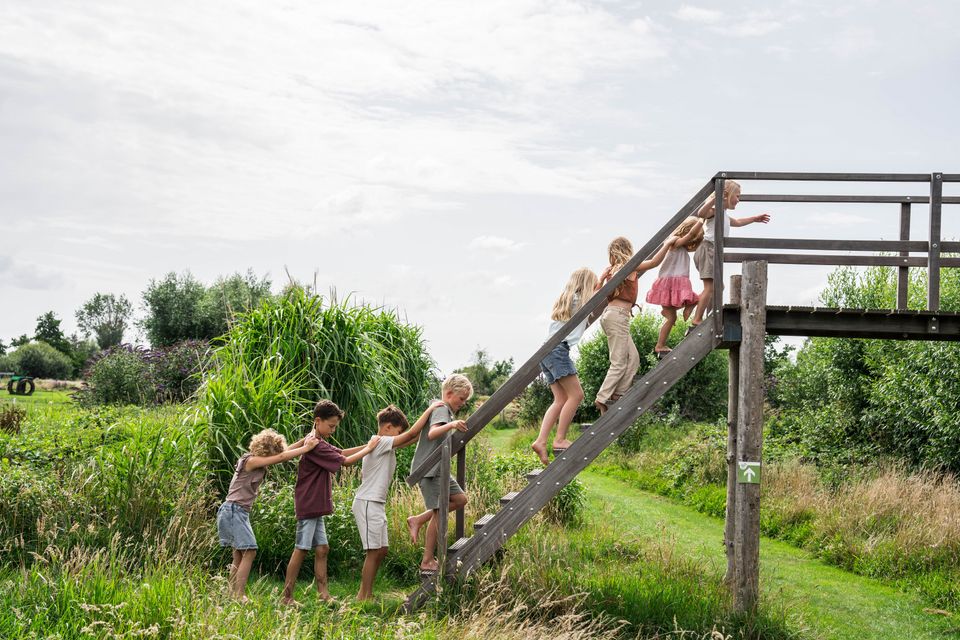 Recreatieplek Buitenplaats Kameryck in Kamerik, Groene Hart, kinderen lopen op blote voeten over houten brug in het blotevoetenpad met groen landschap en speelnatuur.