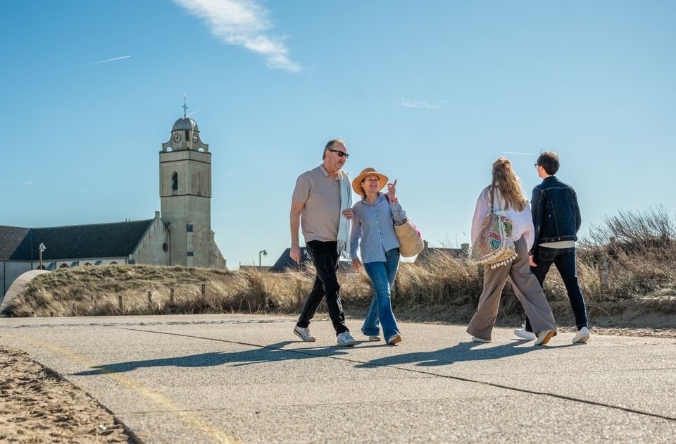 Een man en vrouw wandelen door de duinen in Katwijk aan Zee, met op de achtergrond de Witte Kerk, ook Andreaskerk genaamd.