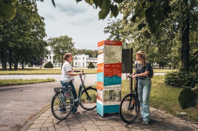 Twee vrouwen bij een TOP informatiebord met op de achtergrond Paleis Soestdijk in Baarn op De Utrechtse Heuvelrug.