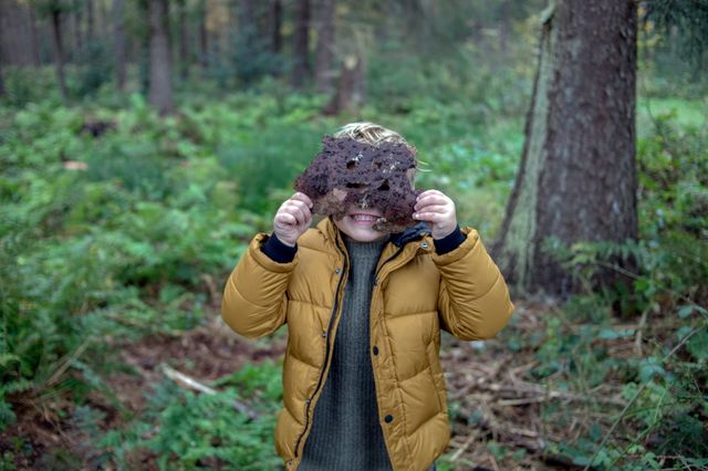 Een jongetje staat in het bos en houdt twee bladeren voor zijn hoofd.
