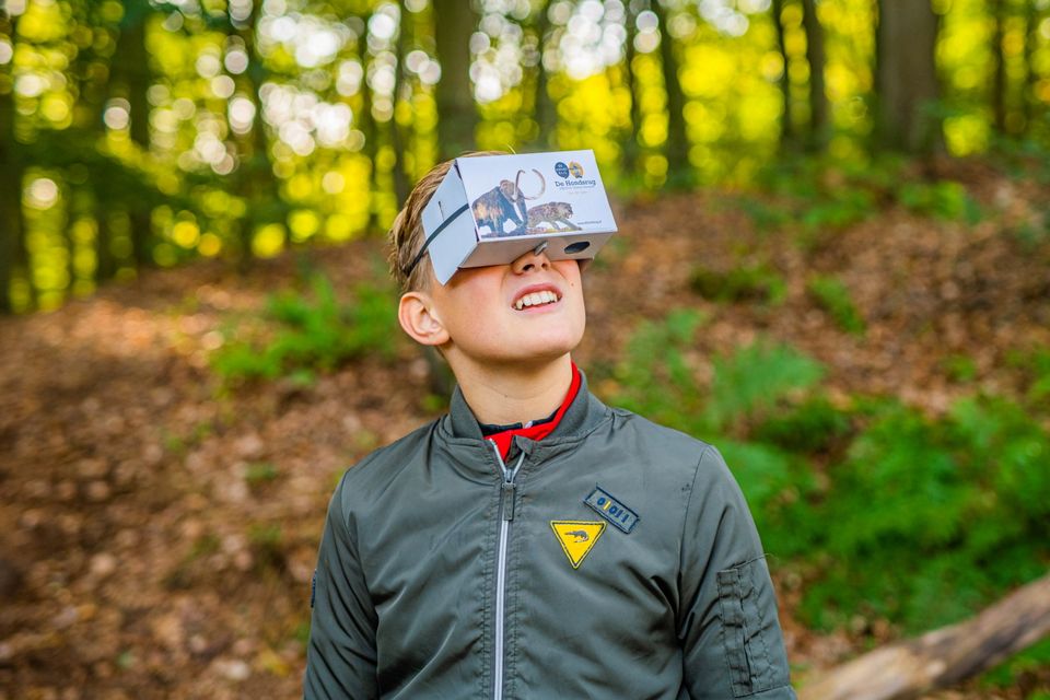 Een jongen staat in het bos met een VR-bril op.