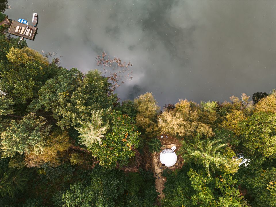 Dronefoto van bosgebied met een verblijf aan een waterplas met kano's