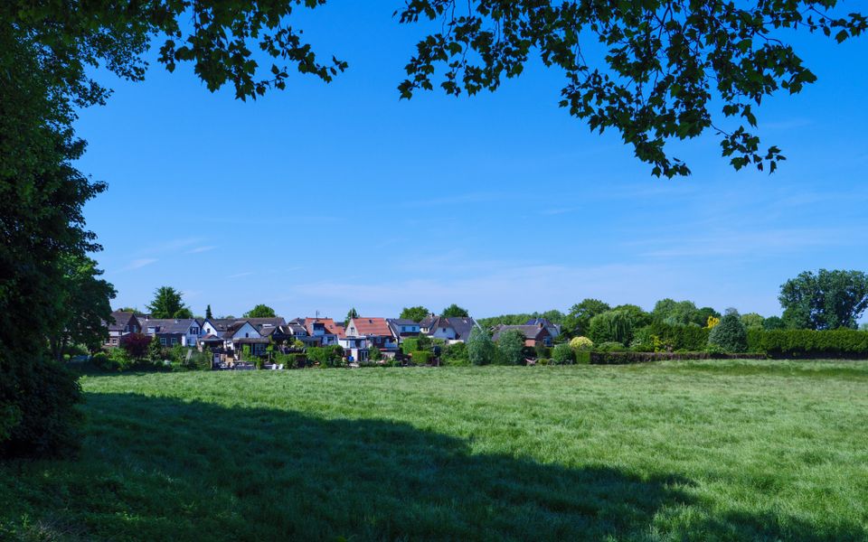 Groen grasveld, blauwe lucht en op de achtergrond een woonwijk