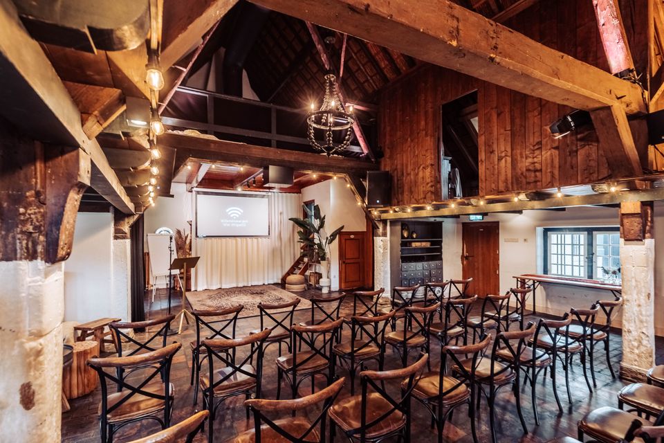 Evenementenlocatie De Willemshoeve in Woerden, Groene Hart. Zaalopstelling met stoelen gericht op presentatiescherm voor vergadering, seminar of zakelijke bijeenkomst in karakteristieke boerderijlocatie.