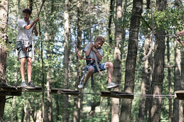 Vader en zoon slingeren in het klimpark van plank naar plank.