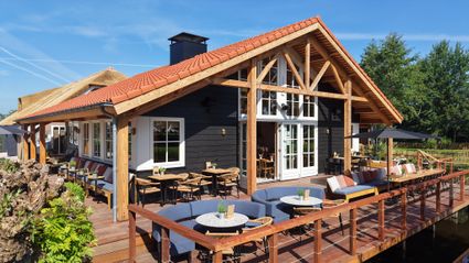 Restaurant De Oortjeshoeve in Kamerik, Groene Hart. Landelijk restaurant met ruim terras aan het water, houten veranda, rieten dak en zitplaatsen buiten op een zonnige dag in het Utrechtse polderlandschap.