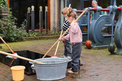 Jongetje en meisje met zwabber en teil met water in de tuin van het Fries Scheepvaart Museum