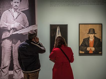 een man en een vrouw luisteren door een apparaatje terwijl ze de schilderijen bekijken van jopie huisman