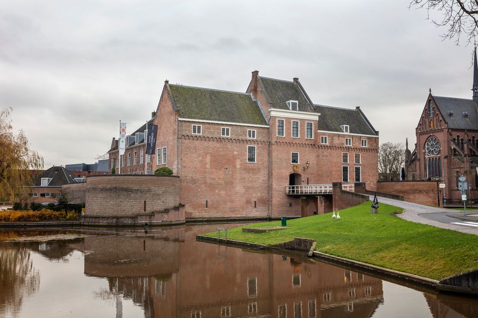 Historisch Kasteel Woerden met rode bakstenen muren en ophaalbrug, omgeven door een gracht en weerspiegeling in het water, gefotografeerd op een grijze herfstdag.