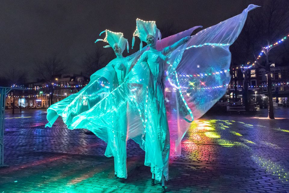 Tijdens de lichtjeswandeling in Woerden zweven verlichte figuren door de avond. Hun kleurrijke kostuums en dansende stoffen brengen magie en verwondering in de historische binnenstad.