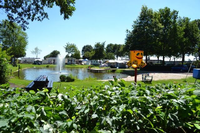 Kindvriendelijke camping met vijver, fontein, speeltoestellen en tenten op een zonnige dag bij Camping De Meije in het Groene Hart.