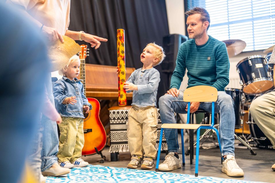 Muziekschool Muziekhuis in Oudewater, Groene Hart, ouder- en peutermuziekles met jonge kinderen die samen muziek maken met instrumenten in een muziekruimte met gitaar, piano en drumstel.