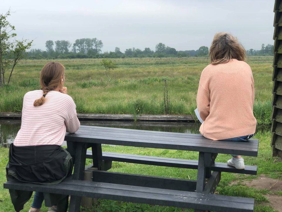 Twee personen zitten op een picknicktafel en staren naar een weiland.