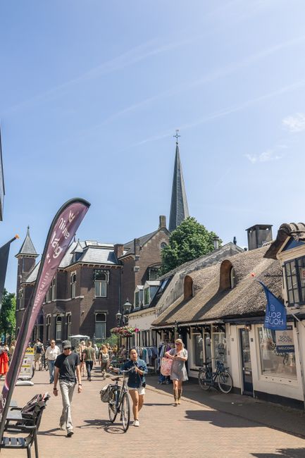 Mensen lopen met fiets aan de hand door dorpskern van Baarn
