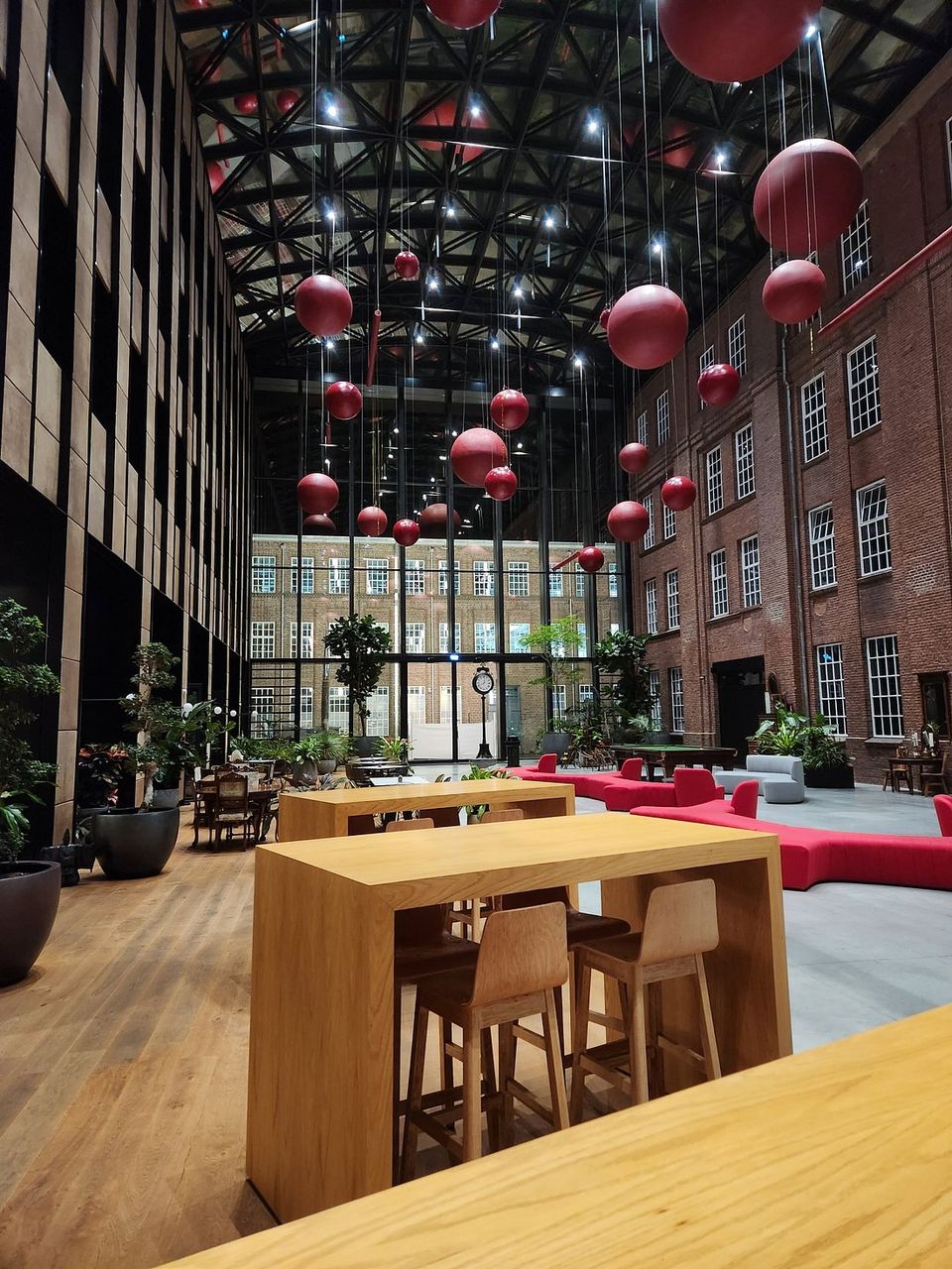 Foto van een met glas overdekte open ruimte (atrium) in het donker. Zichtbaar zijn de ramen van de hotelkamers in de gevel links en rode banken en hoge tafel in het midden.
