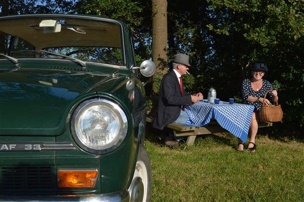 Een stel zit te picknicken aan een tafel naast hun Daf.