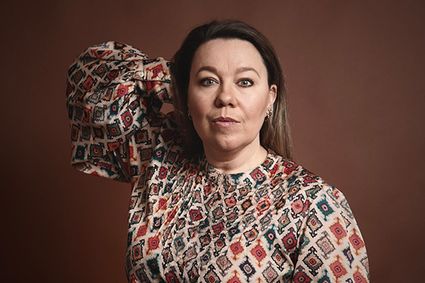 Promotieportret van zangeres Esther Groenenberg voor een optreden in theater Het Klooster in Woerden, Groene Hart, met close-up van de artiest in een kleurrijke patroonjurk tegen een warme bruine studioachtergrond.