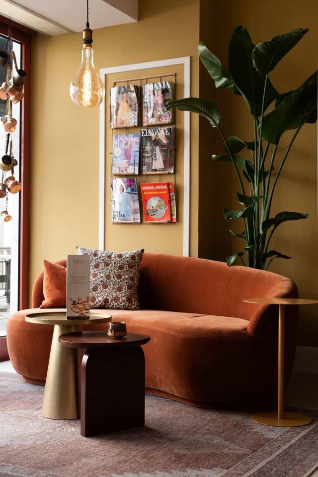 Een huiskamersetting met een comfortabele bank, koffietafels, planten en magazines aan de muren.