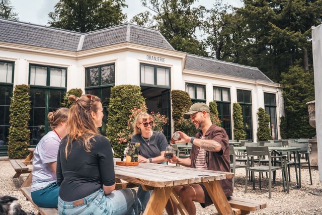 Een groep vrienden drinkt een drankje bij de orangerie van Paleis Soestdijk