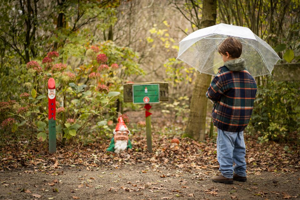 Jongetje staat met een paraplu voor een kabouter, in het bos