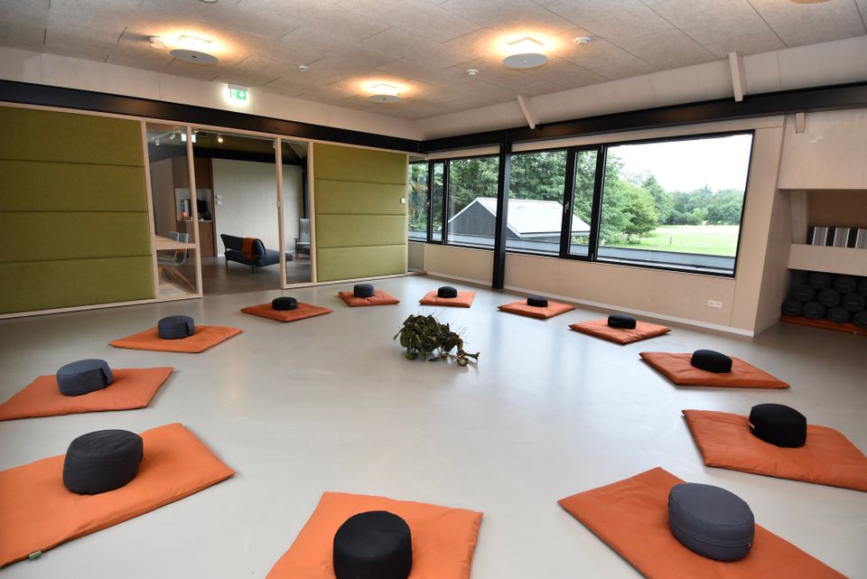 Een lichte ruimte met op een witte vloer oranje matjes en zwarte kussentjes.