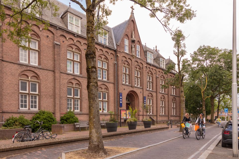 Theater Het Klooster in Woerden, Groene Hart, gevestigd in een monumentaal voormalig kloostergebouw, met fietsers die langs de historische bakstenen gevel rijden.