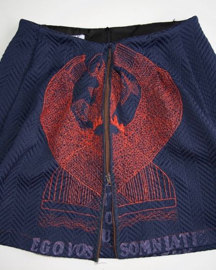 Donkerblauwe handgemaakte rok met rood borduursel en tekst “Ego Vos Somniate”, onderdeel van een textielkunstwerk binnen de expositie.