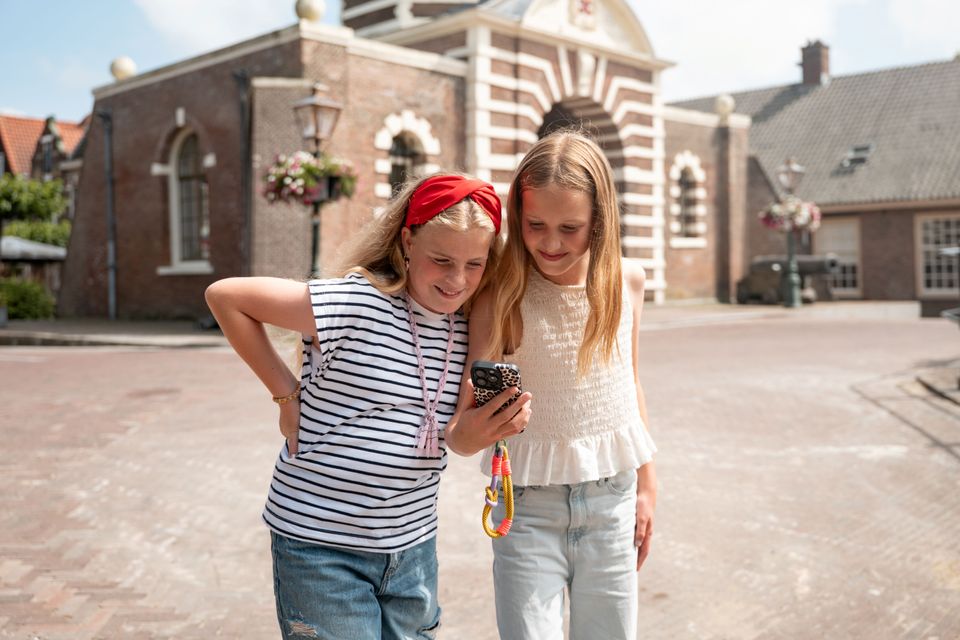 Twee kinderen luisteren met telefoon naar de familie audiotour. Ze staan voor de Leidse Morspoort, één van de stops op de route.