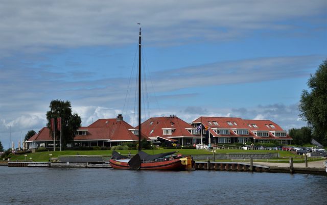 een gebouw met bruine dakpannen een een zeilboot aan de kant.