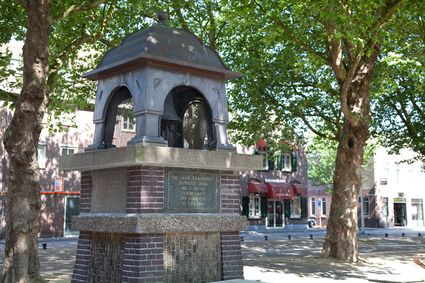 De Kaasbel op het Kerkplein in Woerden, een monument ter ere van 100 jaar kaasmarkt, omringd door bomen en historische panden.