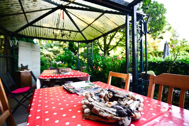 Sfeervol overdekt terras in een groene tuin in Renswoude, met tafels, stoelen en decoratieve details. De foto laat een rustige plek zien om iets te drinken of te eten in een landelijke omgeving.