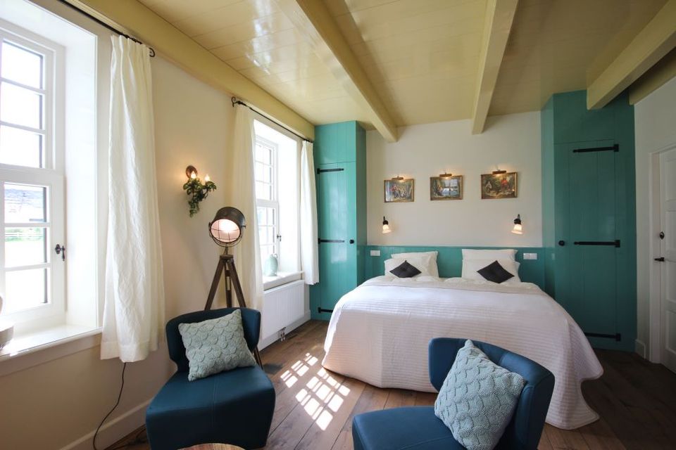 Tweepersoonsbed met twee blauwe stoelen ervoor