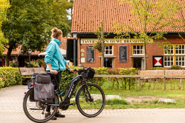 Een fietser die voor Taverne Oude Brandtoren stilstaat met de fiets in de hand.
