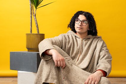 Theatervoorstelling Breek de Week met Ayoub Kharbach in Het Klooster, Woerden, Groene Hart, portret van Ayoub Kharbach zittend in een studio-opstelling met gele achtergrond ter promotie van de voorstelling.