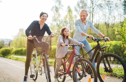 Gezin met vader, moeder en dochter fietst samen over een zonnig pad in het groen; ze lachen en genieten van een ontspannen fietstocht in de natuur.