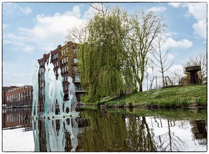 Openluchtkunstwerk Singelkunst Woerden, Woerden, Groene Hart, transparante silhouetbeelden geplaatst in het water van de stadssingel met moderne bebouwing en groen op de achtergrond.