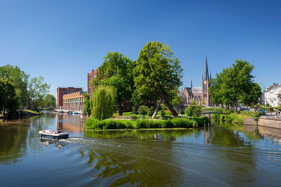 Sloep op de Singel in Woerden, historische vestingstad in het Groene Hart, met uitzicht op Defensie-eiland en de Bonaventurakerk tijdens een zonnige vaartocht door de binnenstad.