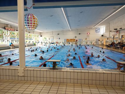 Kinderen en volwassenen zwemmen baantjes tijdens de Zwem4daagse in zwembad Batenstein in Woerden, omringd door vrolijke versieringen en toeschouwers.