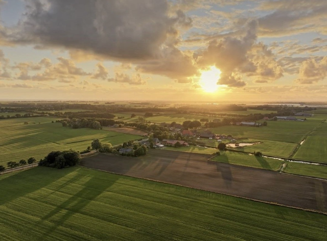 Een dronefoto van een dorp in Friesland met een laaghangende zon.