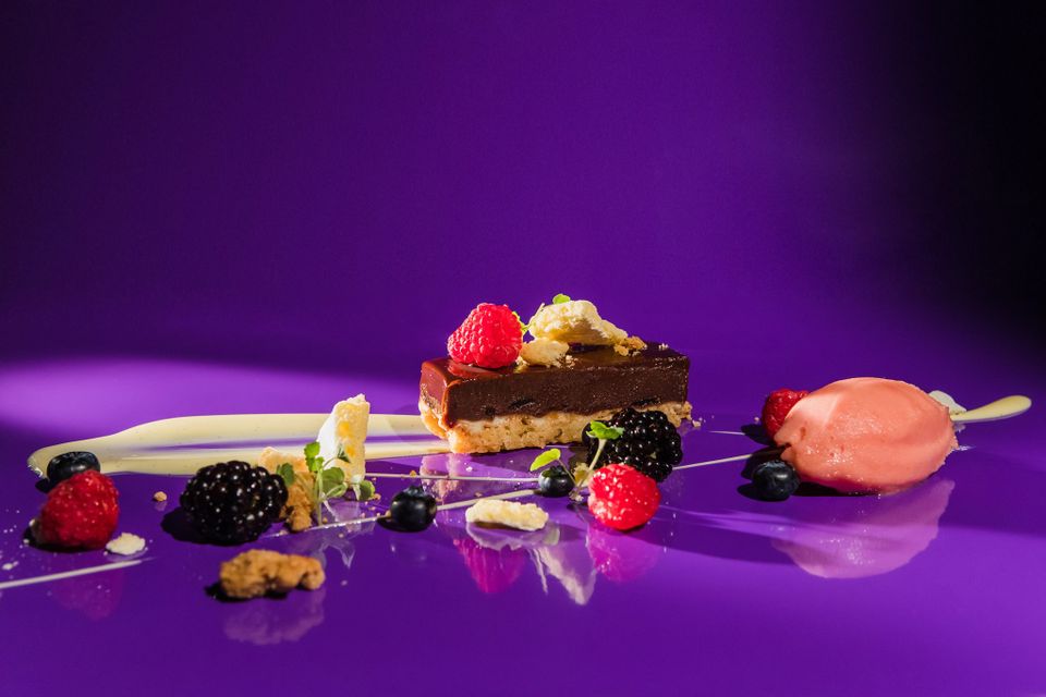 Geraffineerd dessert bij restaurant De Heeren van Montfoort met chocoladegebak, sorbet en vers rood fruit, stijlvol gepresenteerd op een paarse achtergrond.