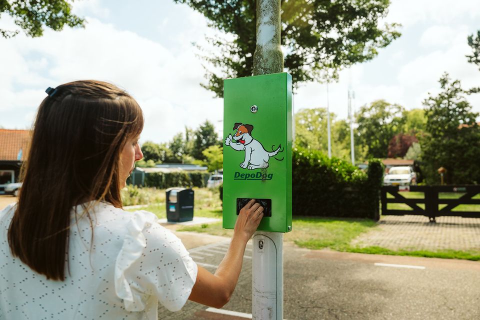 Vrouw pakt hondenpoepzakje uit dispenser langs de openbare weg