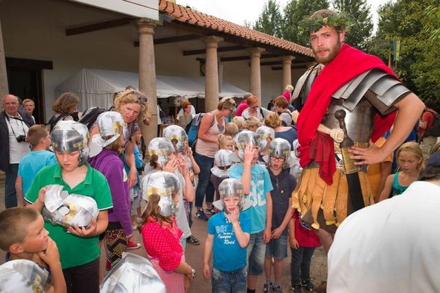 Kinderen met Romeinse helmen doen mee aan een interactieve workshop onder begeleiding van een Romeinse soldaat in Archeon, tijdens een educatief familie-uitje in het Groene Hart.