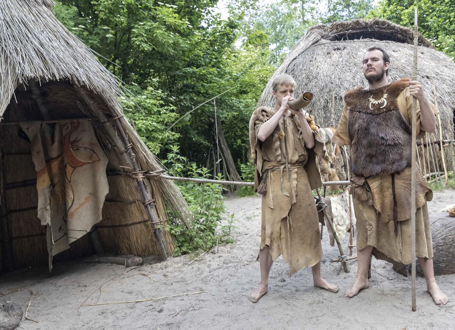 Twee mannen in prehistorisch klederdracht voor twee rieten hutjes