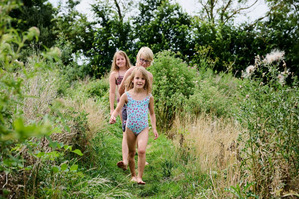 Een jongen en twee meisjes die in het gras in hun zwemkleding achter elkaar aan lopen op het blotevoetenpad de Hege Gerzen met veel groen op de achtergrond.